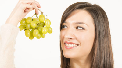 Young woman holding up a bunch of green grapes, smiling.