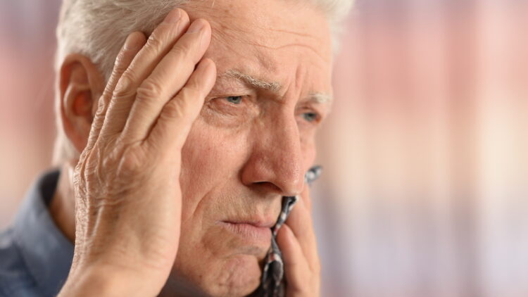 Elderly man with his hand on his head, holding his tooth in pain