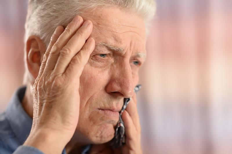 Elderly man with his hand on his head, holding his tooth in pain